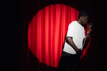 Jazz singer african american man sings song holding retro microphone in hands on stage with red curtains