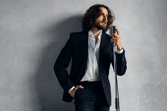 Portrait of handsome attractive singer in classic suit on grey background. Happy Man singing pop hit in retro microphone