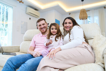 Pregnant mother and father relaxing on sofa with daughter