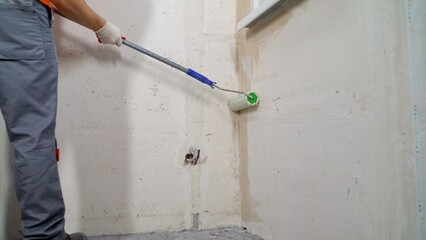 Construction worker applying waterproofing coating on wall with roller