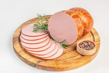 Sliced bologna sausage on a wooden board with rosemary and colorful peppercorns
