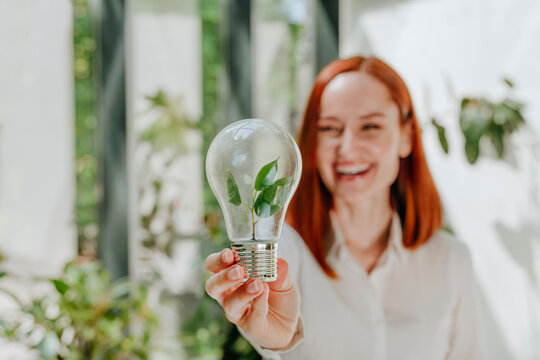Smiling businesswoman holding light bulb with leaves in office