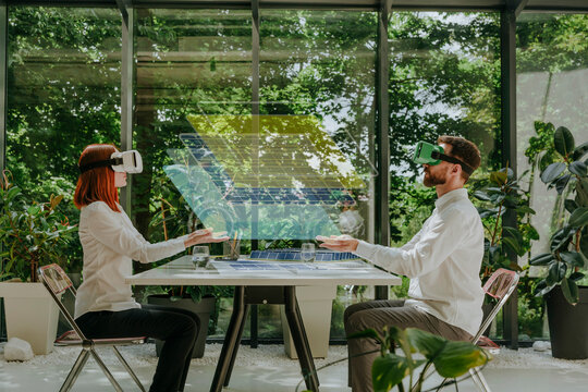 Engineers wearing virtual reality simulators designing solar panels in office