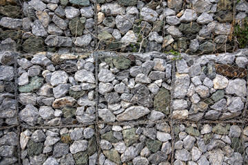 gabion wall, showcasing the texture of the grey stones and the wire mesh. The image highlights the detailed pattern and rugged nature