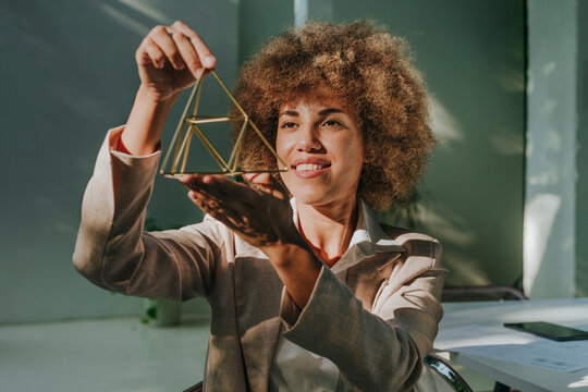 Happy businesswoman examining metal pyramid in office