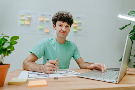 Web designer sitting with laptop and printout at desk in office