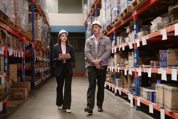 Distribution warehouse manager and client businesswoman using digital tablet checking inventory storage on shelf. Storehouse business worker and logistic engineer standing together at storage service