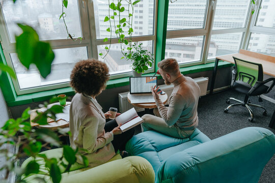 Multiracial colleagues discussing graph on laptop in meeting at coworking office