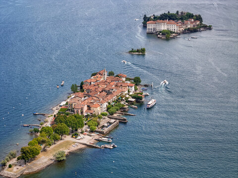 Aerial view of terracotta rooftops cascade across Isola dei Pescatori as boats glide on the cobalt waters towards Isola Bella, Isola Superiore, Piemonte, Italy.