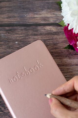 Hand is holding pencil on top of notebook placed on wooden table. Top view.