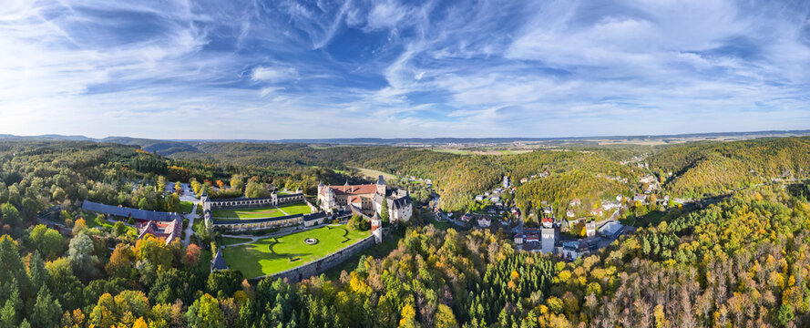 Aerial view of the majestic Rosenburg Castle embraces verdant grounds, framed by a tapestry of autumn-hued forests under a vast, streaked sky, Rosenburg, Lower Austria, Austria.