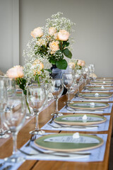 Stylish dining table arranged with white plates, champagne flutes, and delicate floral centerpiece on rustic wood. Perfect setting for wedding reception, private event, or special gathering.