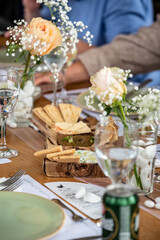 Close-up of assorted dips with pita bread served in rustic wooden bowl on decorated wedding table with roses, water glasses and guests enjoying intimate celebration meal.