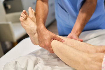 Therapist providing elderly patient with leg massage during rehabilitation session