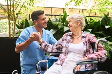 Smiling caregiver assisting senior woman in wheelchair at outdoor rehabilitation center