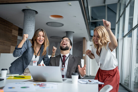 Excited business team celebrating success at work using laptop