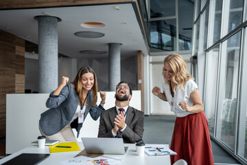 Business team celebrating success around laptop in modern office