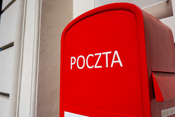 Red mailbox with 'Poczta' text against a wall in Warsaw, Poland