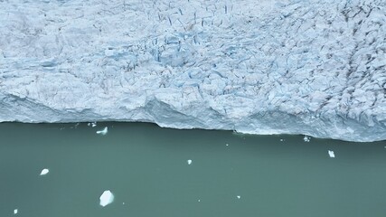 Aerial view of a colossal glacier meeting the teal waters, dotted with white icebergs, creating a stunning juxtaposition of textures and hues, Chile.