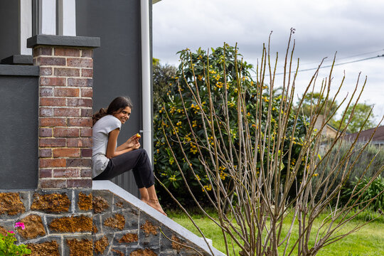 tween girl sitting on steps of home eating a loquat from the tree in the garden
