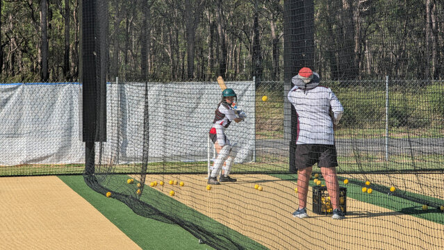 Middle-aged person throwing cricket balls to young female batter