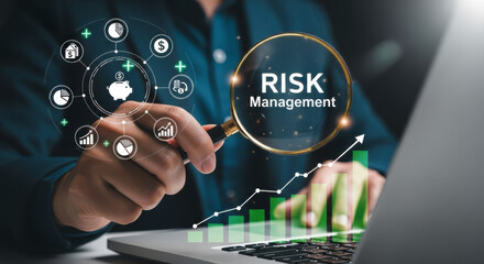 Man wearing a suit using a magnifying glass to view "RISK Management" text, with glowing financial charts and pie graphs, on a laptop, illustrating financial analysis