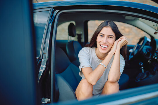 Happy tourist sitting in a car with an open door, smiling and laughing during a joyful road trip adventure through the beautiful countryside - Powered by Adobe