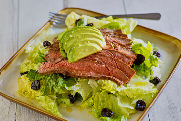 mixed green salad topped with sliced flank steak, avocado, and black olives, rotated