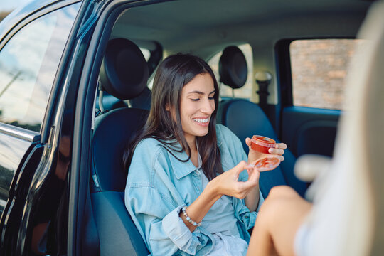 Happy tourist is eating sauce from a small plastic container while sitting on a passenger seat of a car during a road trip