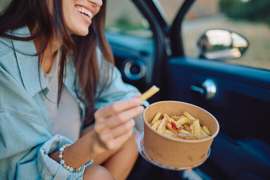 Happy woman enjoying chips while relaxing in a car, savoring a delicious road trip snack during a well-deserved break