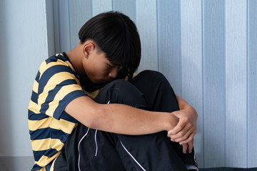 Teen boy sitting on the floor with head down, hugging knees, feeling sad and depressed. Concept of...