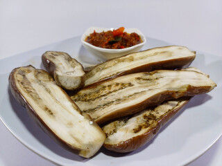 A dish of cooked eggplant slices, served with a vibrant red chili sauce, presented on a rectangular white plate. Suggests a savory, flavorful, and spicy meal, characteristic of Southeast Asian cuisine