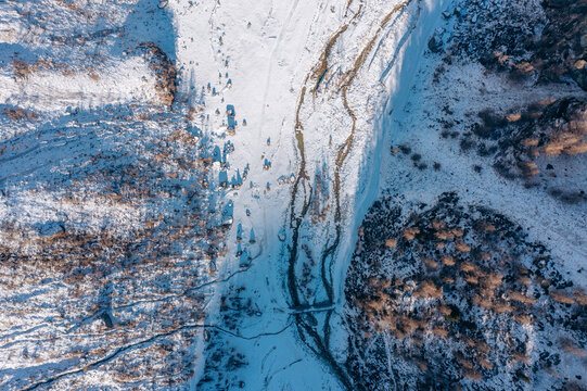 Aerial view of a snow-covered landscape bisected by a meandering stream, with snow-laden trees casting shadows, Zinal, Valais, Switzerland.
