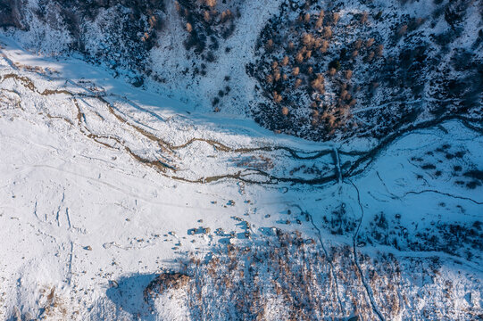 Aerial view of a winding river snaking through a snow-laden valley, contrasting sharply with the dark, dense trees clinging to the mountainside, Zinal, Valais, Switzerland.