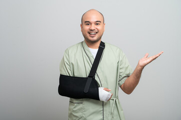 Asian man in patient attire smiles gently at the camera, wearing an arm sling and bandage, striking different poses to show resilience and a positive attitude during recovery.