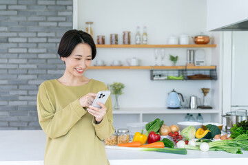 キッチンでスマホを使うミドルの主婦 © pain au chocolat