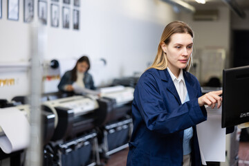 Woman using printer while working in print shop. Female printshop worker using printing device, pushing buttons.