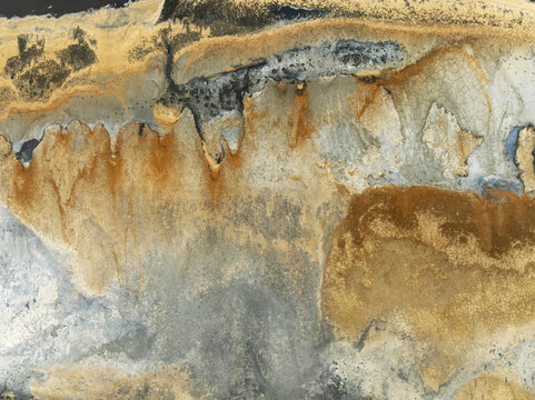 Aerial view of mineral deposits creating a textured landscape with gold, gray, and black hues, resembling abstract art, Walvis Bay, Erongo region, Namibia.