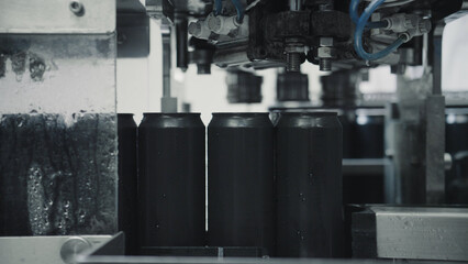 Automated machinery sealing black aluminum cans in a beverage or food processing factory, emphasizing industrial automation and manufacturing efficiency