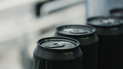 Freshly produced black aluminum beverage cans are rolling on a production line, covered with condensation, indicating they are cold and ready for distribution
