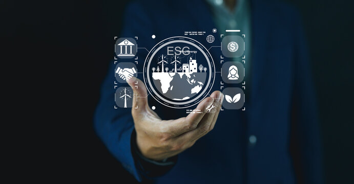 A businessman holds a holographic digital interface displaying ESG (Environmental, Social, Governance) icons with global and financial symbols.