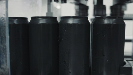 Black aluminum cans glistening with condensation are traveling along a conveyor belt in a beverage production factory, highlighting the efficiency of modern industrial manufacturing processes