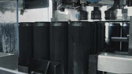Black aluminum cans are moving on a conveyor belt, entering a filling and sealing machine in a beverage production factory, showcasing the automated process of drink packaging