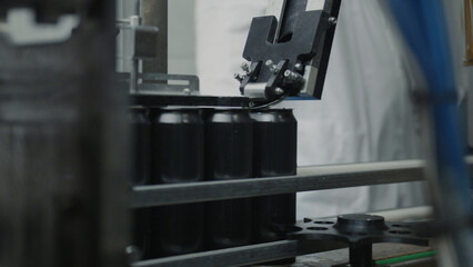 Automated machine is handling black aluminum cans on a conveyor belt, representing the efficiency and precision of modern beverage production processes within a factory setting