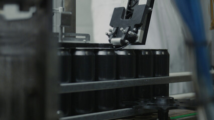 Robotic arm is expertly placing black aluminum cans onto a conveyor belt within a beverage production facility, showcasing the automation of the canning process