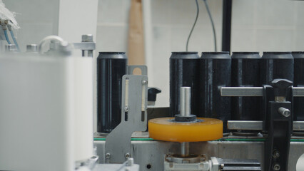 Black aluminum cans moving on a conveyor belt are being labeled and processed by a machine in a beverage factory, showcasing the automated production process