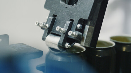 Automated industrial machinery applying tops to metal beverage containers, optimizing production in a modern factory setting, showcasing advanced manufacturing technology