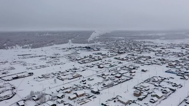 Aerial view of a snow-covered landscape with scattered houses and a forest, the white expanses contrasting with the dark roofs, Oymyakon, Sakha Republic, Russia.