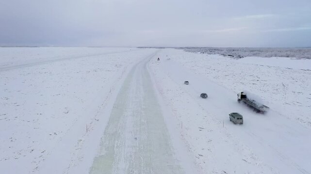 Aerial view of vehicles traversing a snow-covered road, cutting through a vast, icy expanse under a muted sky, Yakutsk, Sakha Republic, Russia.
