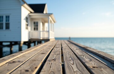 A wooden pier extends towards a white seaside house with a view of the ocean under a clear sky